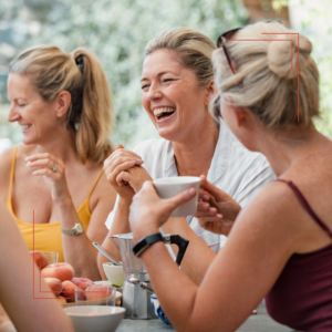 Vier Frauen in den Wechseljahren sitzen draußen am Tisch, lächeln und unterhalten sich, lachen und sind glücklich.